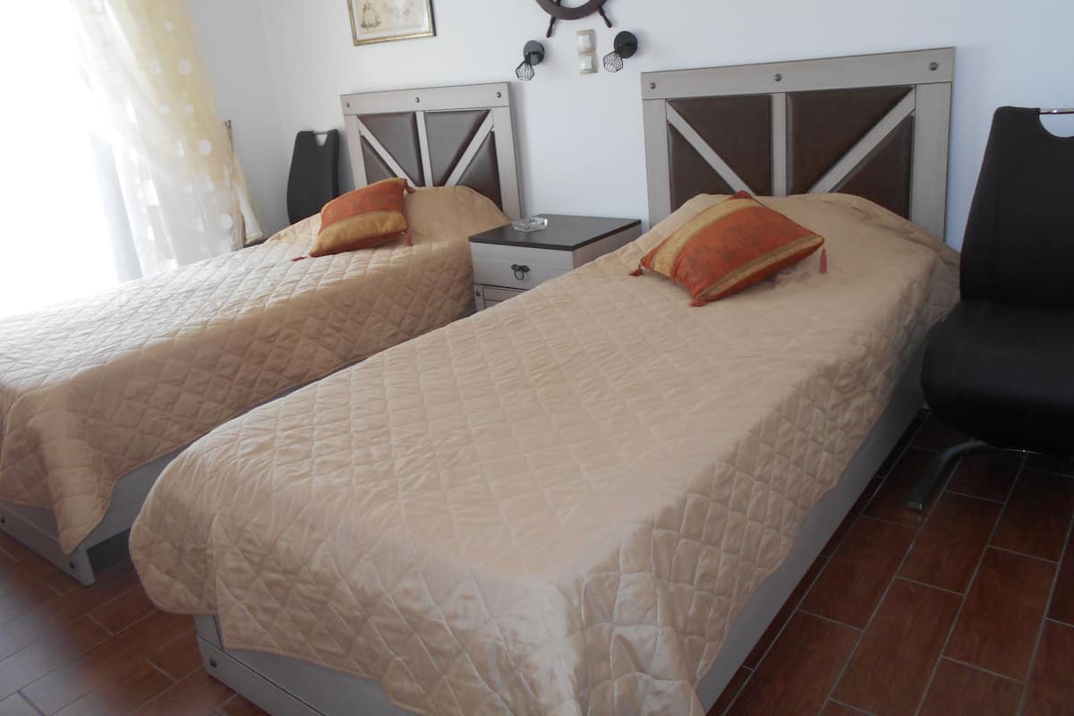 Two beds with headboards, a nightstand, a chair, and a wall with a ship's wheel and a picture.