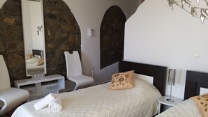 A bedroom with two beds, a stone wall, a mirror, a chair, and a bedside table. - La Veranda of Mykonos (Mykonos)