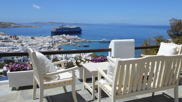 A balcony with white chairs and a table overlooking a coastal town with a cruise ship in the distance. - La Veranda of Mykonos (Mykonos)