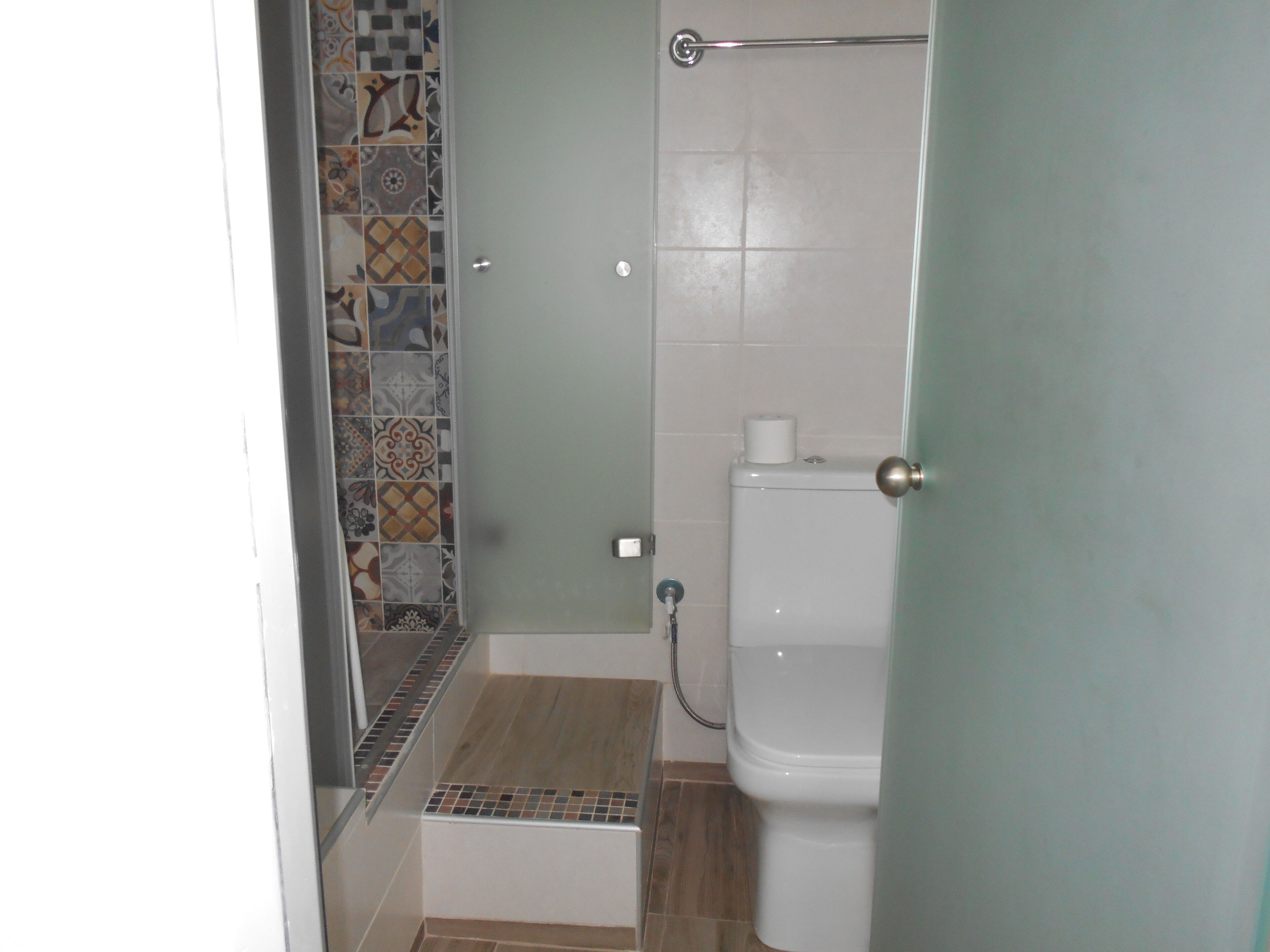 A bathroom with a shower, toilet, and a tiled wall.