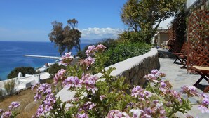 A coastal view with a stone wall, outdoor seating, and flowering plants. - La Veranda of Mykonos (Mykonos)