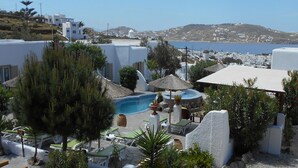 A resort with a pool area, lounge chairs, and a view of the sea and distant hills. - La Veranda of Mykonos (Mykonos)