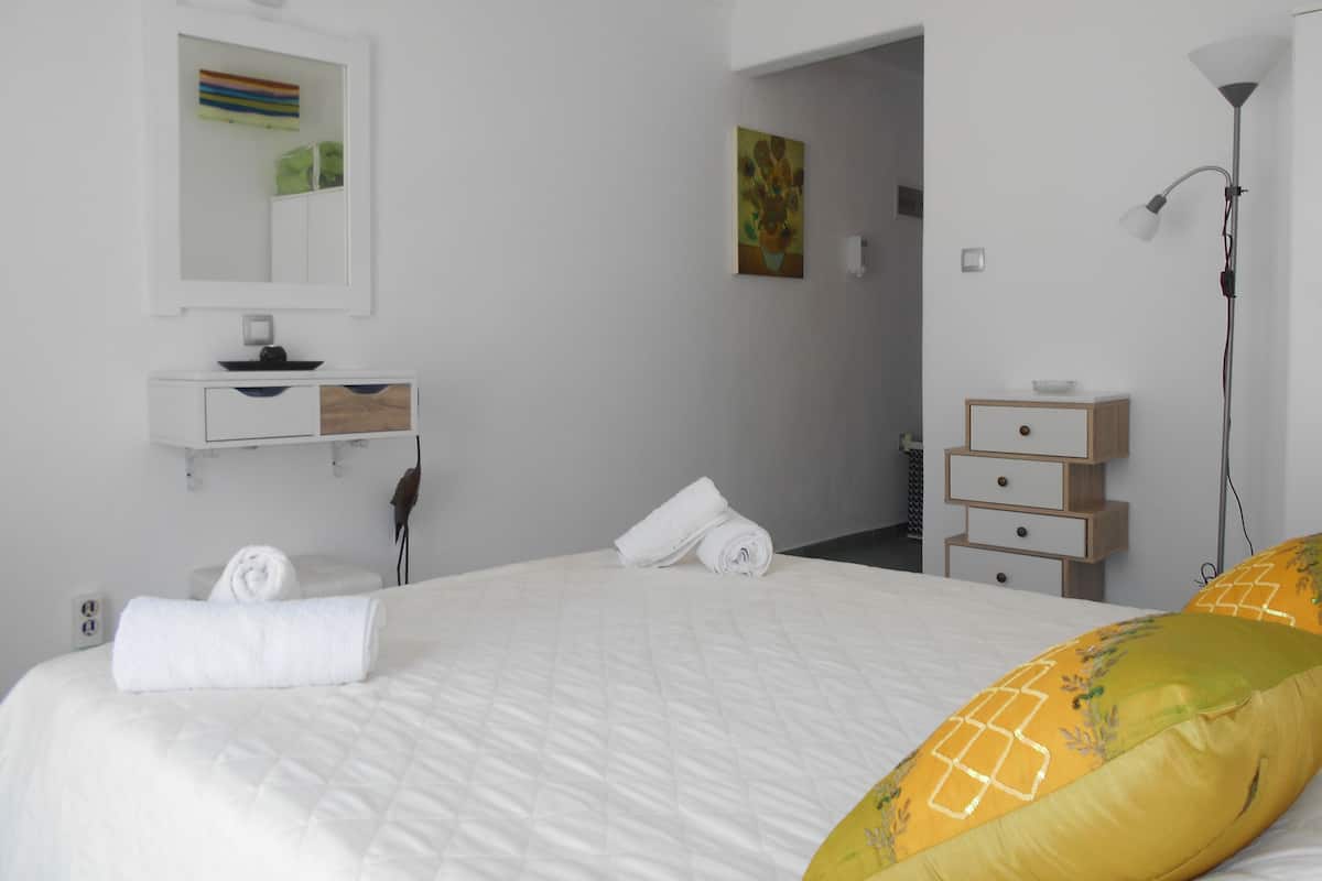 A hotel room with a bed, a bedside table, a mirror, a dresser, and a lamp.