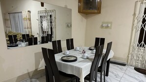 Un coin repas avec une table dressée pour six personnes, entourée de chaises, d’un miroir et d’une fenêtre avec des rideaux.