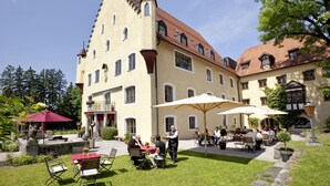 A courtyard with outdoor seating, a large building with a tower, and a well-maintained garden. - Schloss zu Hopferau (Hopferau)