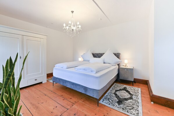 Un dormitorio con cama, candelabro, mesita de noche, armario y planta.