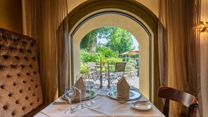A dining table set with white tablecloth, plates, glasses, and napkins, with a view of an outdoor garden through an arched window. - Schloss zu Hopferau (Hopferau)