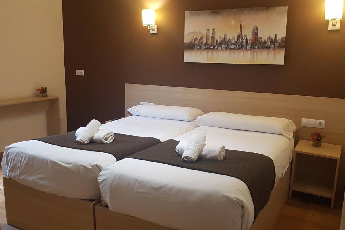 Hotelkamer met een tweepersoonsbed, twee nachtkastjes, een stadsgezicht schilderij en twee wandlampen.
