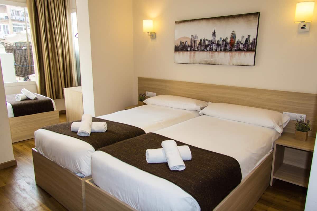 Een hotelkamer met twee bedden, een stadsgezicht schilderij en een raam met gordijnen.
