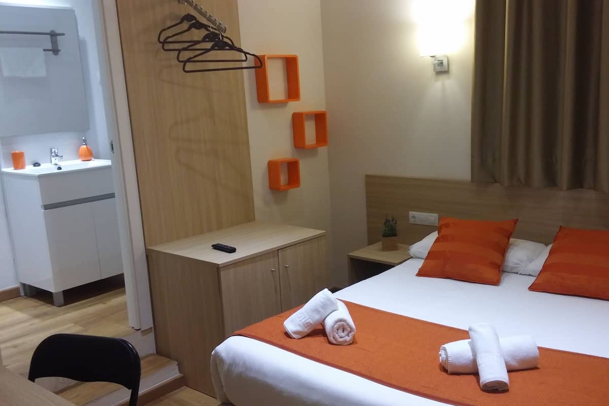 Een hotelkamer met een bed, nachtkastje, een klein tafeltje, een spiegel en een badkamer met wastafel en handdoekrek.