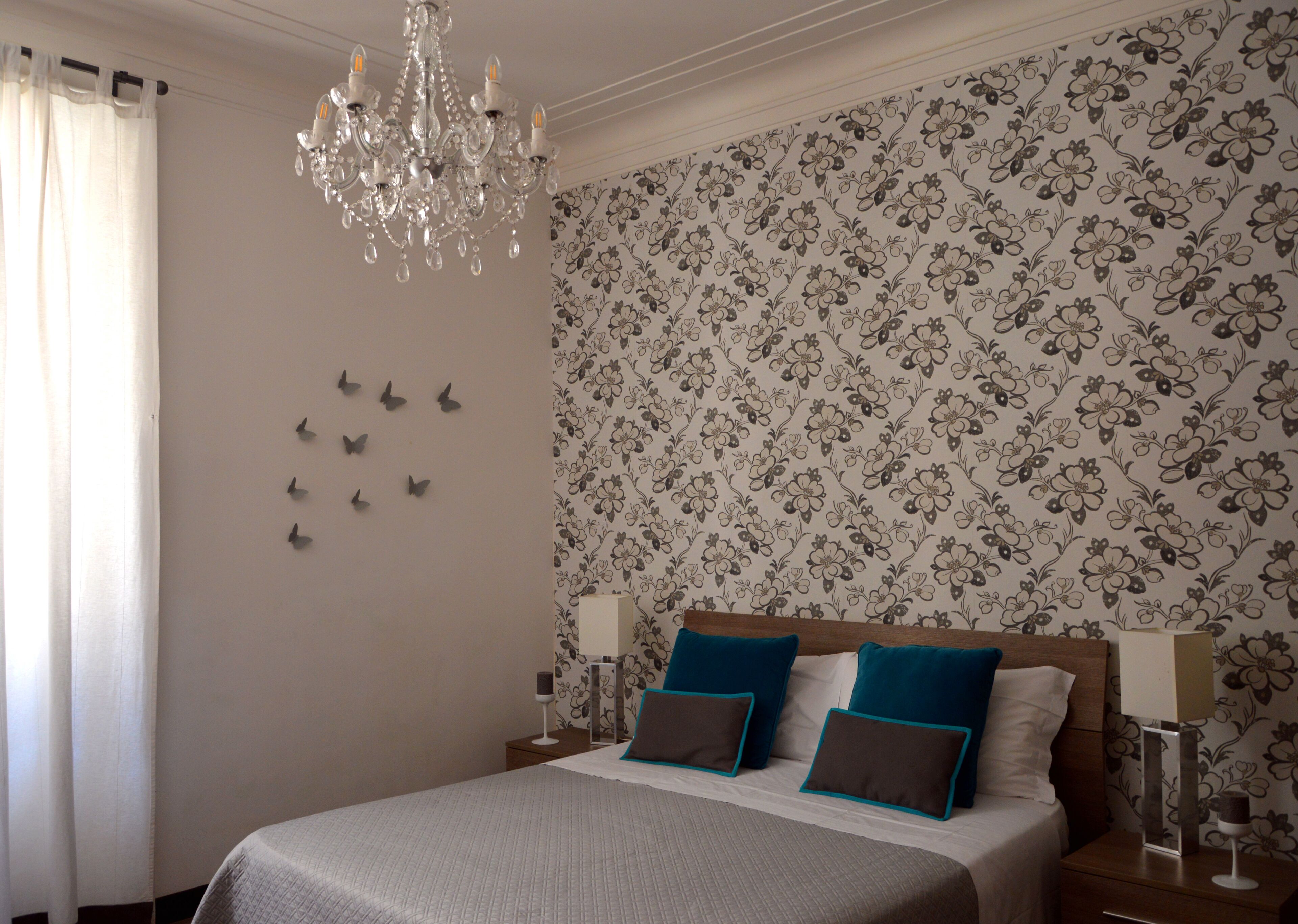 Un dormitorio con una cama grande, un candelabro, papel tapiz floral y adhesivos decorativos de mariposas.