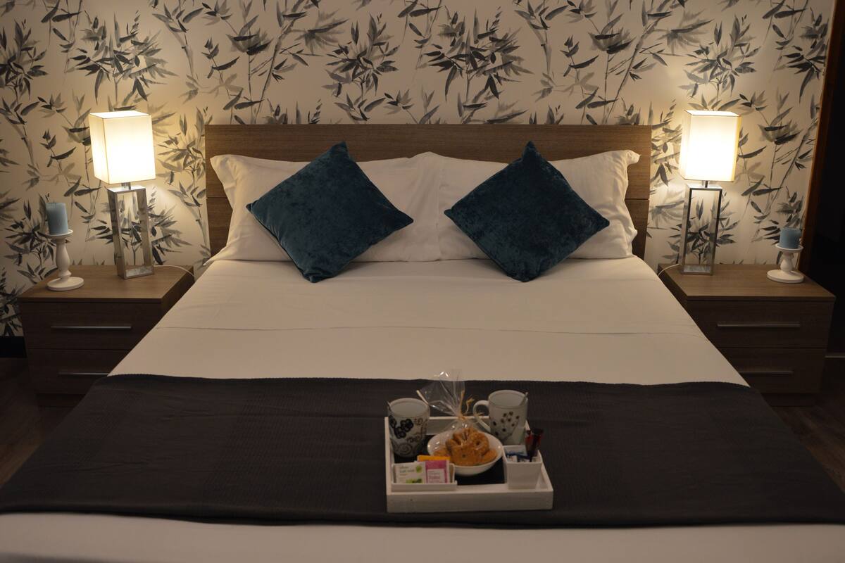 A neatly made bed with two pillows, a tray with breakfast items, and two bedside lamps on wooden nightstands.