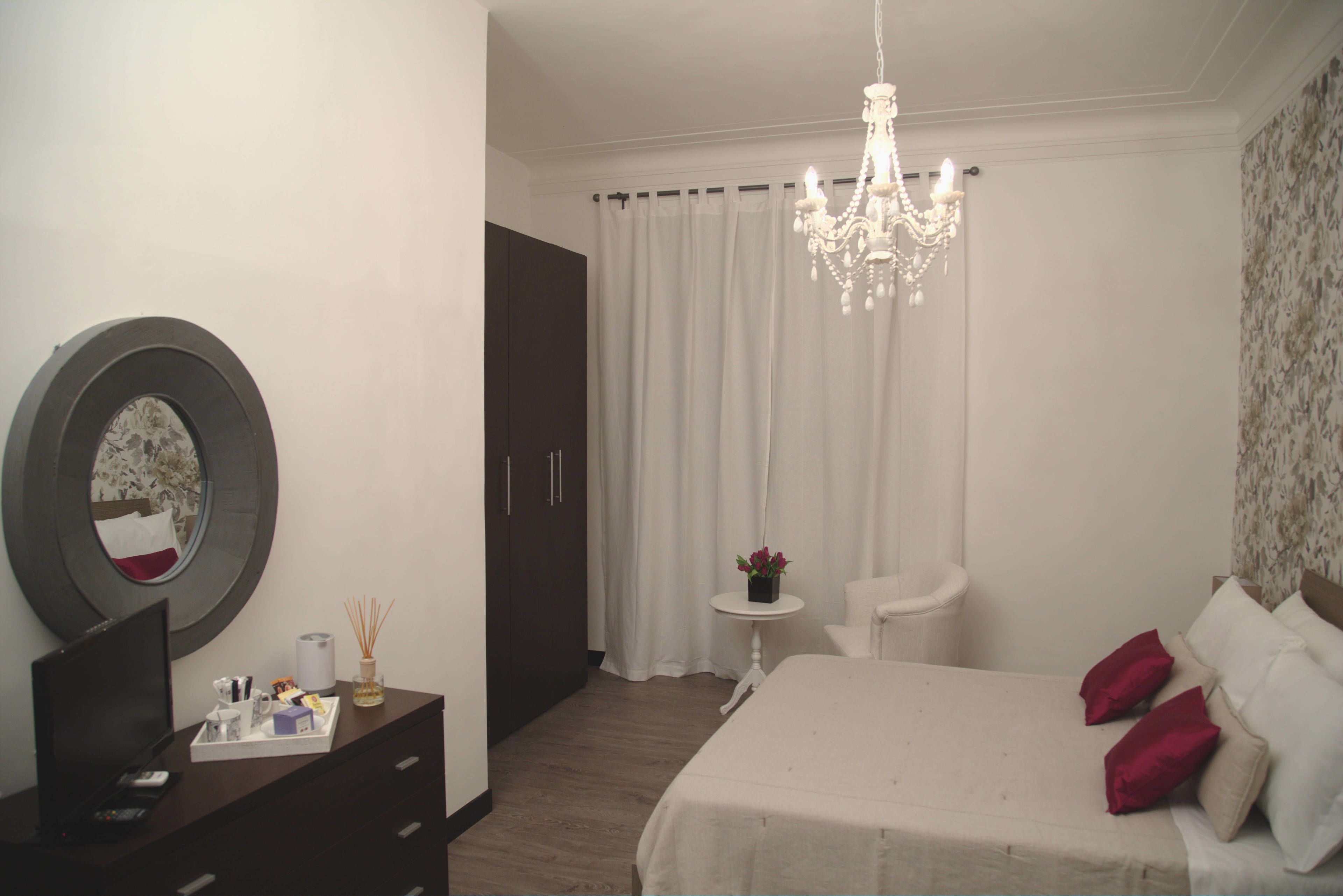 A bedroom with a bed, a desk, a chair, a small table, a mirror, and a chandelier.
