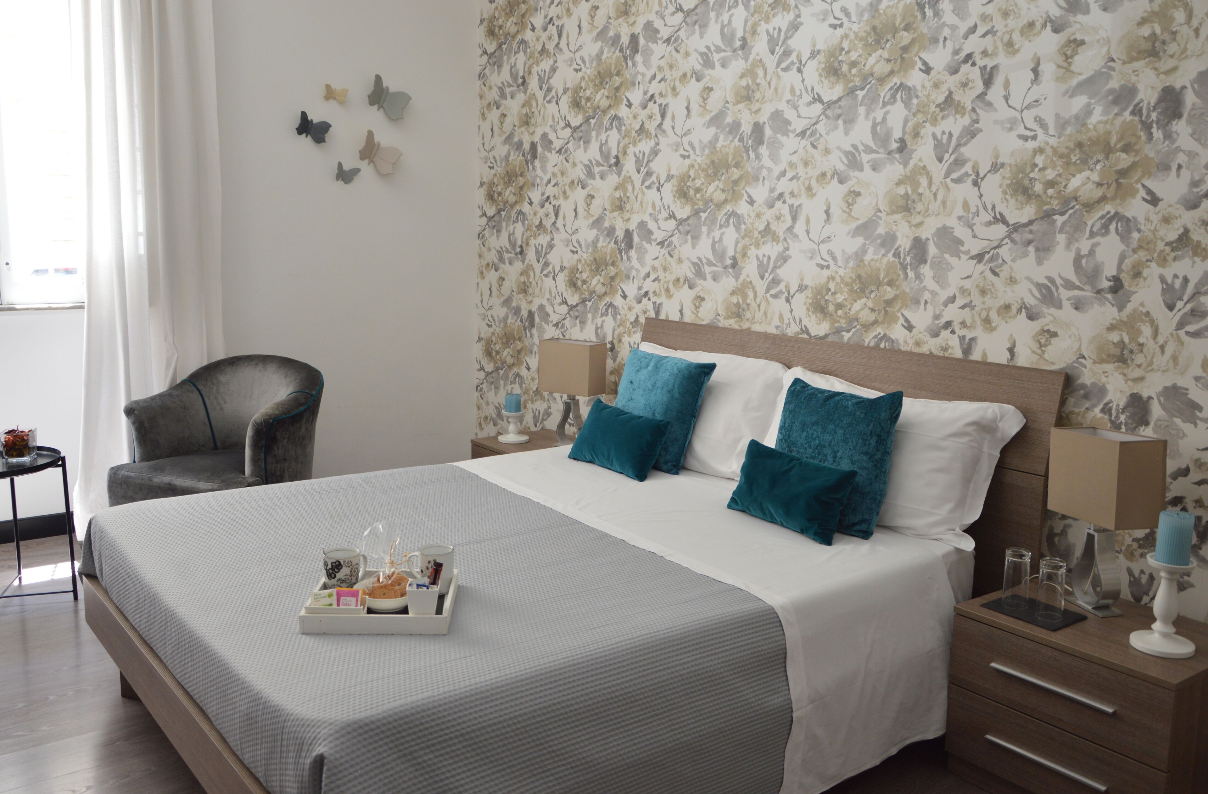 Una cama bien hecha con una bandeja de artículos de tocador, una silla y una mesita de noche con lámpara.