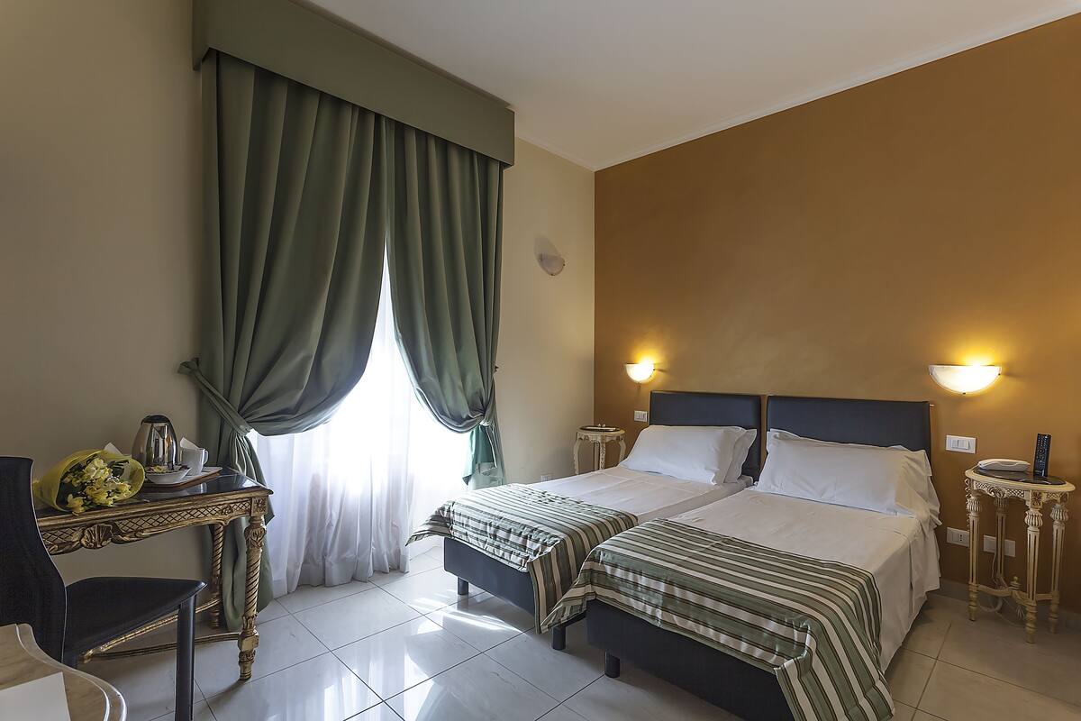 A hotel room with two beds, a desk with a lamp, and a chair.