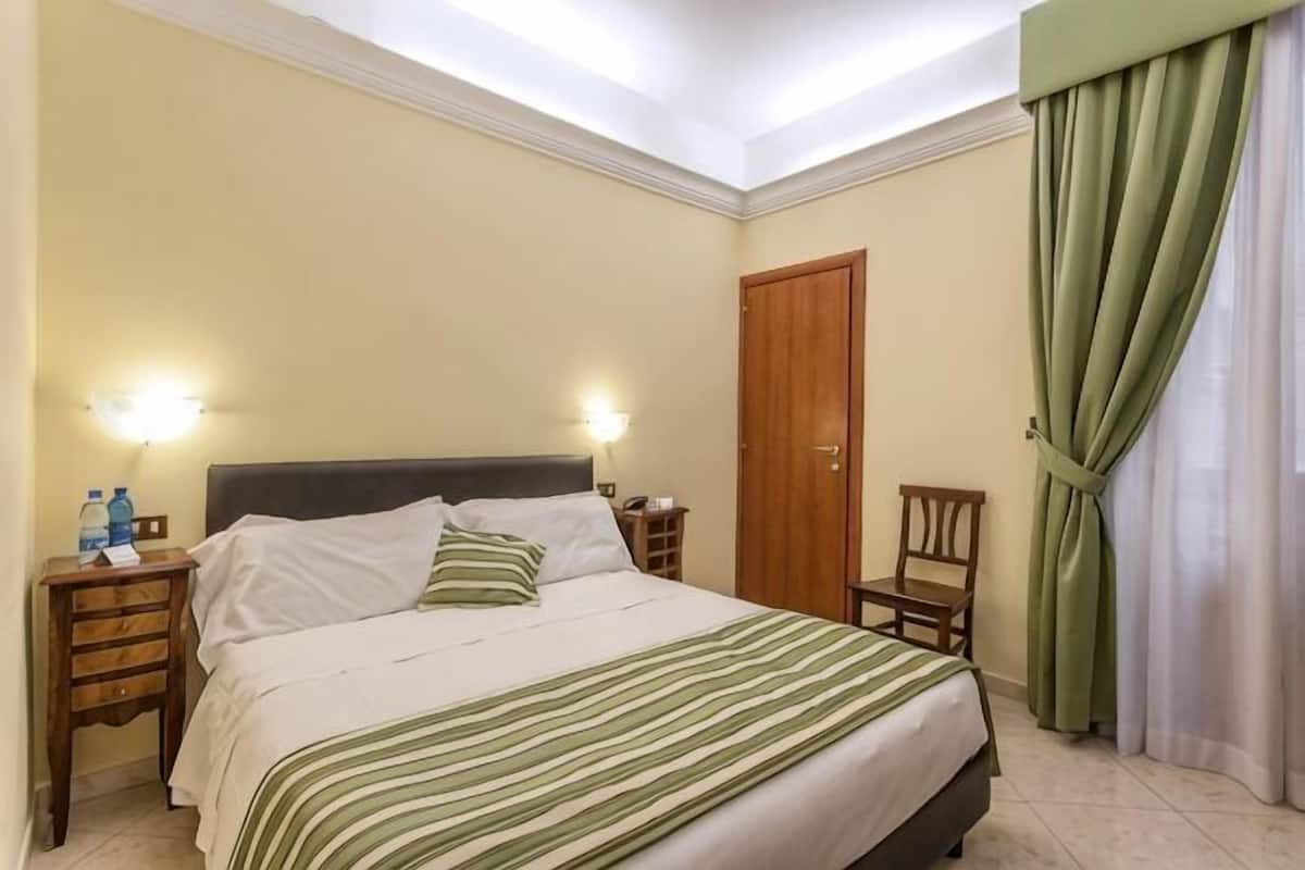 A hotel room with a bed, nightstands, a chair, a door, and curtains.