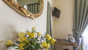 Una habitación con escritorio, una silla, un jarrón con flores amarillas, un espejo y un televisor en la pared.