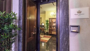 Entrada de hotel con puerta de madera, planta en maceta, alfombra a cuadros y un letrero que dice "Regina Giovanna HOTEL".