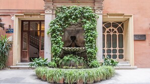 Una entrada de edificio con una fuente, escalones y plantas en macetas.
