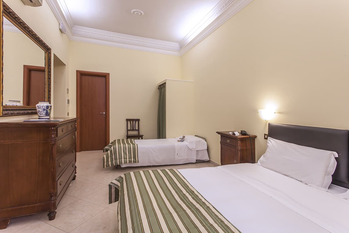A hotel room with a large bed, a smaller bed, a dresser, a mirror, a nightstand, and a lamp.