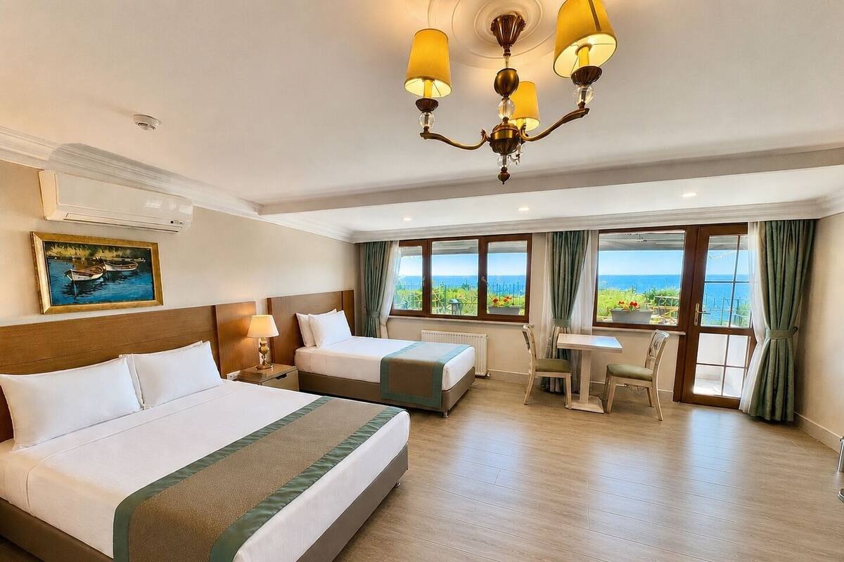 A hotel room with two beds, a dining table, a chair, a chandelier, a painting, and a view of the sea.