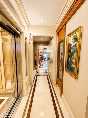 A hotel hallway with a marble floor, an elevator, a staircase, and a painting on the wall.