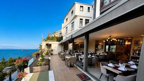 A restaurant with outdoor seating overlooking the sea, a modern interior, and a view of the ocean.