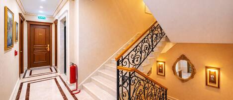 A hotel hallway with a marble floor, a staircase with ornate black railings, a fire extinguisher, and a door marked '204'.