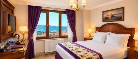 Una camera d'albergo con un letto, una scrivania con una lampada, vista sul mare e un quadro appeso alla parete.