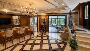 A spacious lobby with a bar area, a chandelier, and a staircase leading to an upper floor.