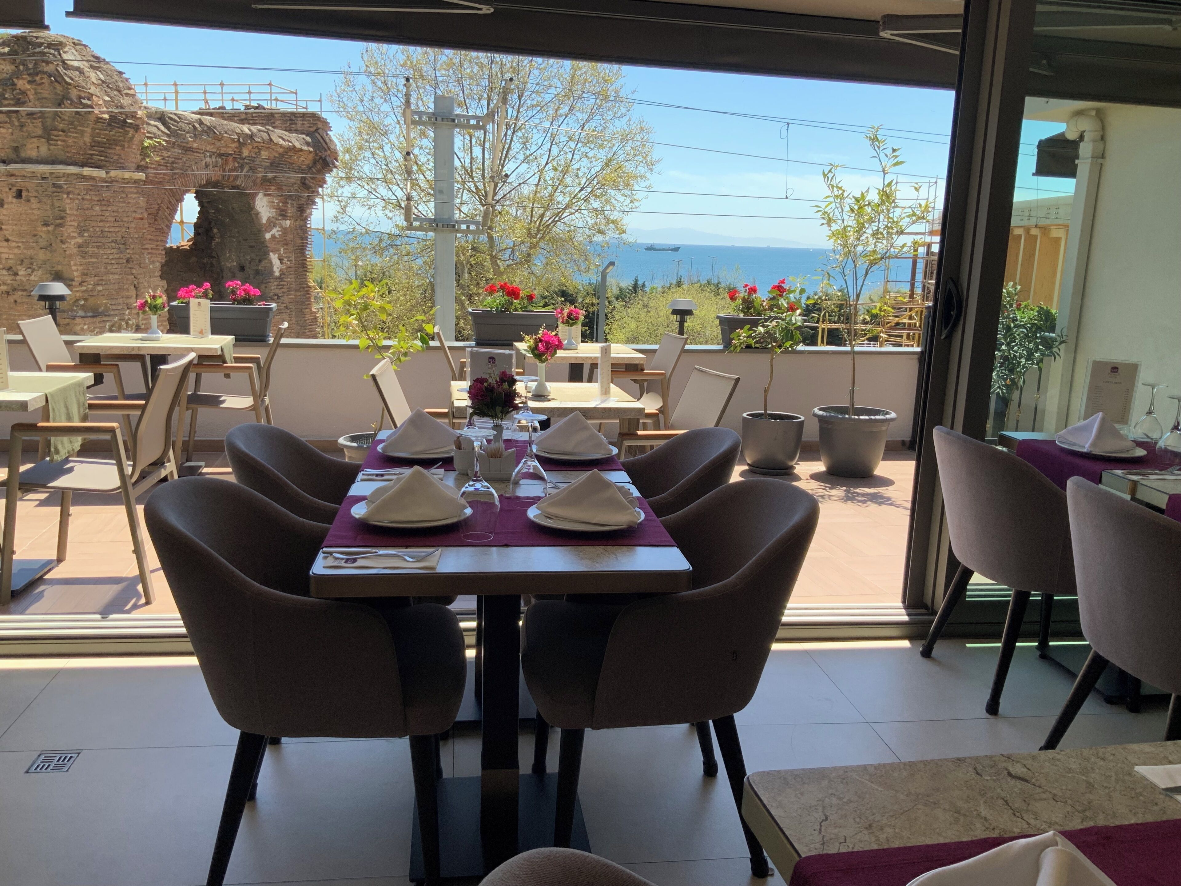 An outdoor dining area with tables set for four, chairs, and a view of the sea and mountains.