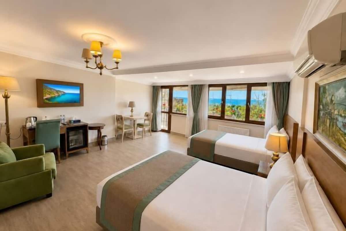 A hotel room with two beds, a desk, a chair, and a view of the sea.