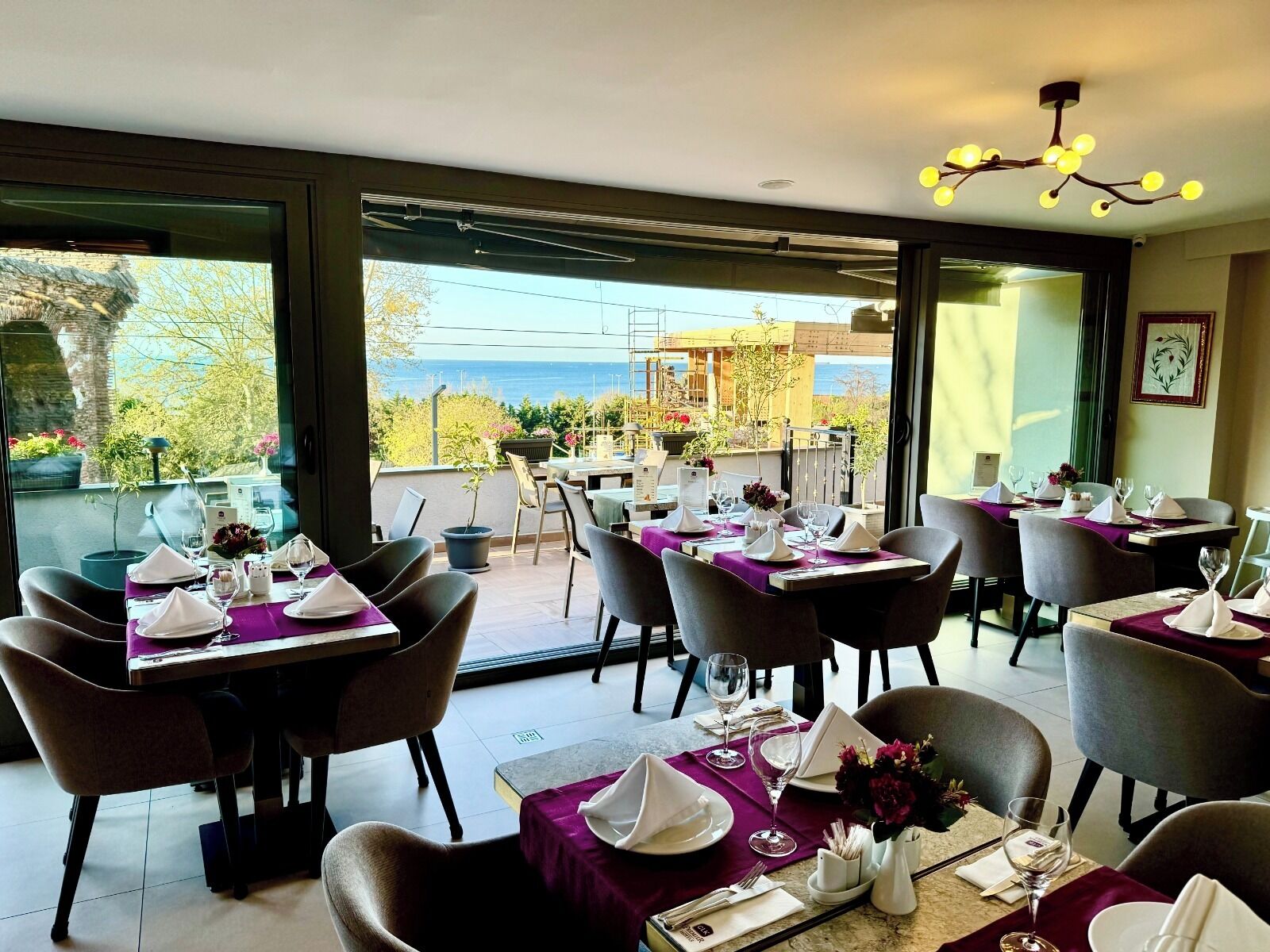 A restaurant with tables set for dining, a view of the sea, and a modern interior design.