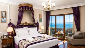 A luxurious bedroom with a four-poster bed, a chandelier, a balcony with a view, and a dining table with fruit.