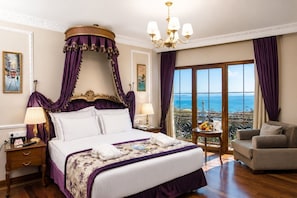 Un dormitorio lujoso con cama con dosel, araña, balcón con vistas y una mesa de comedor con fruta.