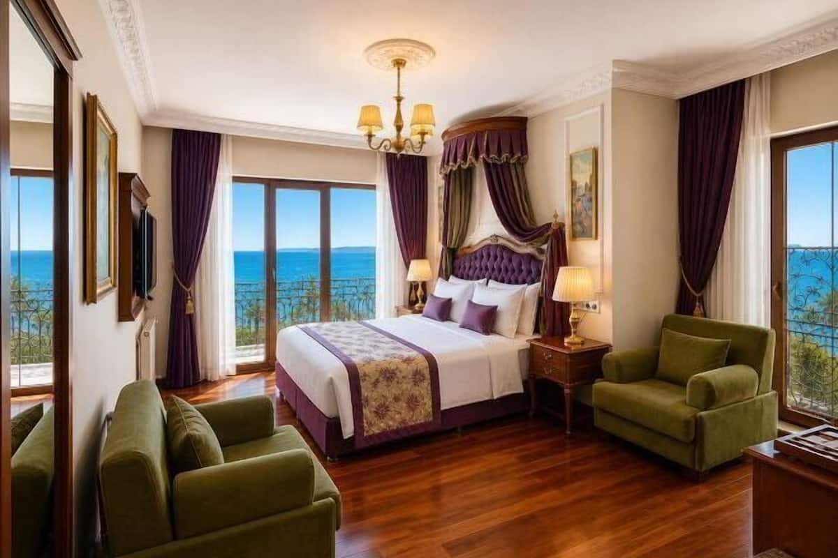 A hotel room with a large bed, two green armchairs, a nightstand with a lamp, and a view of the ocean.