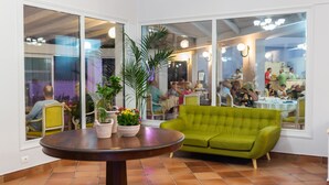 A dining area with a round table, green sofa, and potted plants. - Keri Village & Spa by Zante Plaza - Adults Only - All inclusive (Zakynthos)