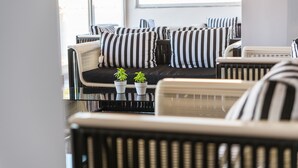 A modern living room with a sofa set featuring black and white striped cushions, two small potted plants, and a glass coffee table. - Keri Village & Spa by Zante Plaza - Adults Only - All inclusive (Zakynthos)