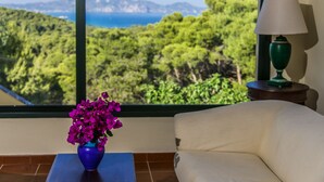 A room with a view of a mountainous landscape, a white sofa, a blue vase with purple flowers, and a green lamp on a wooden side table. - Keri Village & Spa by Zante Plaza - Adults Only - All inclusive (Zakynthos)