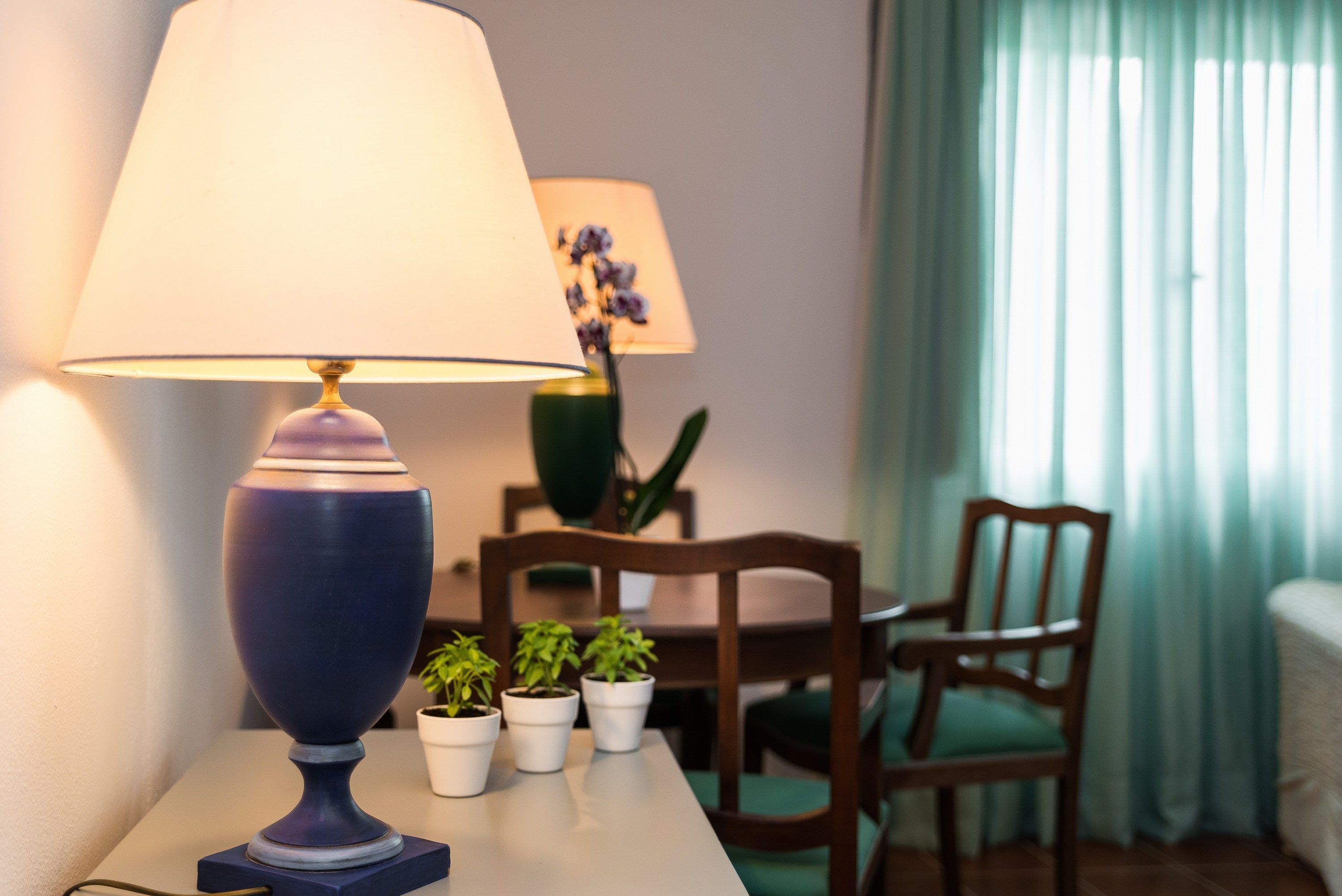 A room with a table, a lamp, a chair, and a potted plant.