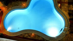 Una piscina con un diseño ondulado único, rodeada de baldosas de piedra y una pequeña luminaria.