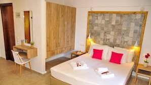 Una habitación de hotel con una cama grande, un armario de madera, un escritorio con silla y una mesita con lámpara.