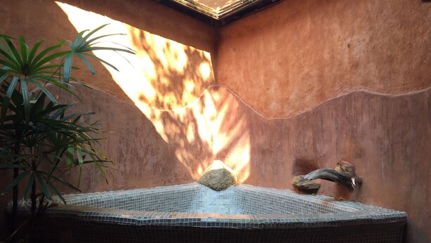 Uma banheira de hidromassagem com azulejos de mosaico, rodeada por pedras e um vaso de planta.