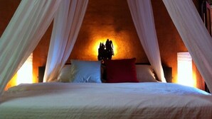 Quarto com cama sob um dossel, mesa de cabeceira com abajur e parede com textura.