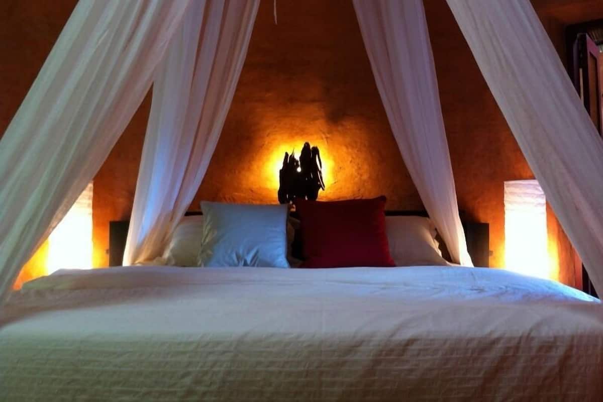 Una habitación con cama bajo un dosel, una mesita de noche con lámpara y una pared con textura.