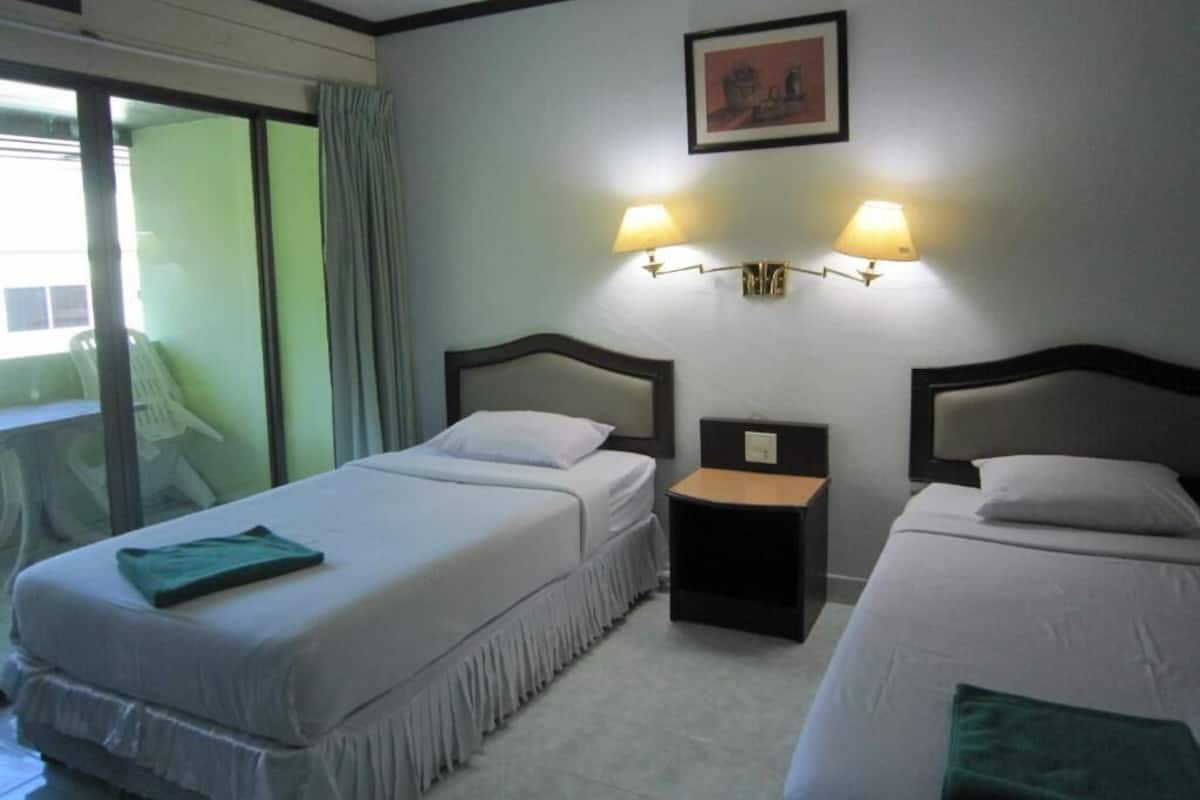 A hotel room with two beds, a small table, and a wall-mounted lamp.