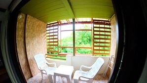 A room with a curved ceiling, a window with wooden slats, two white plastic chairs, and a small table. - PK Mansion (Krabi)