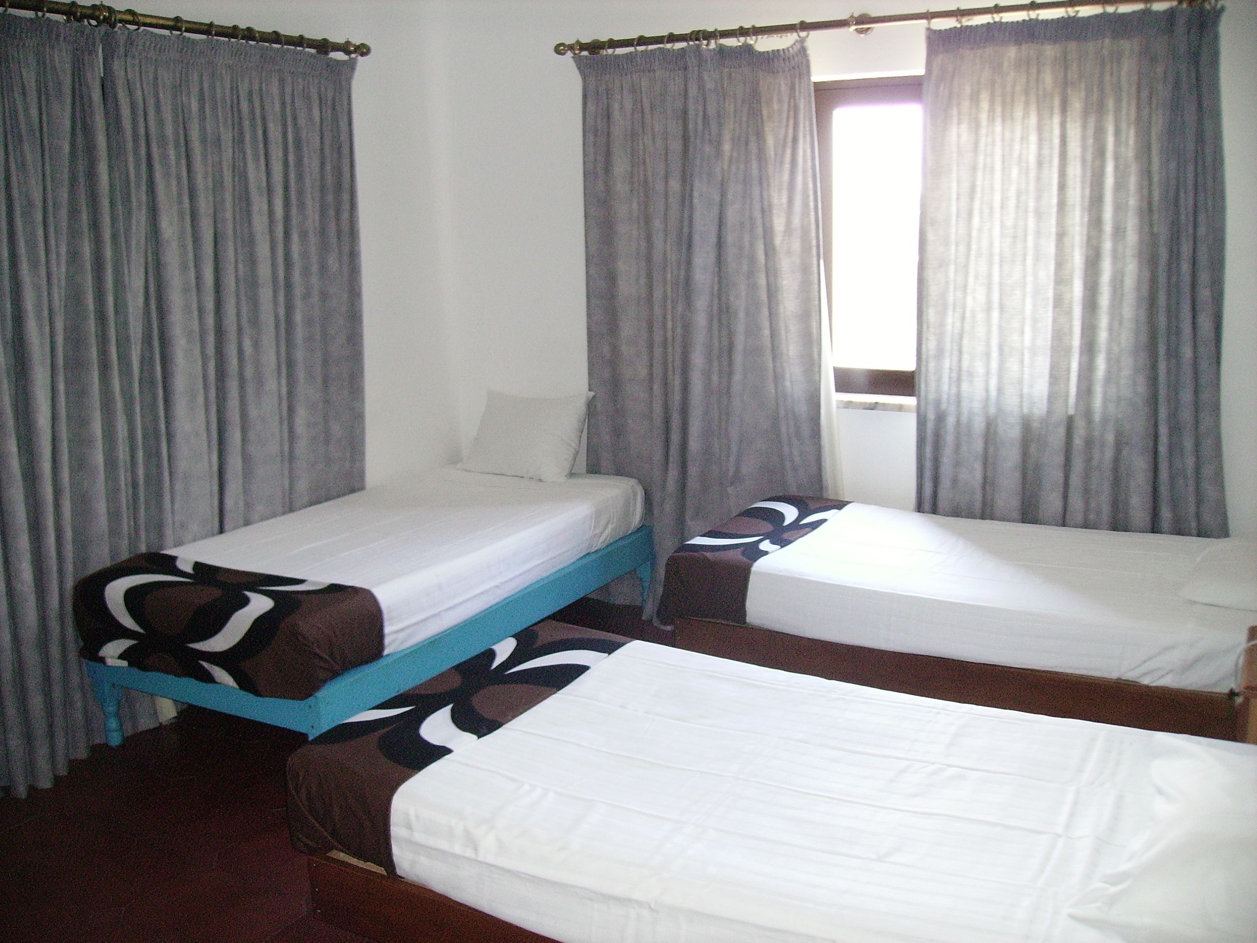 A room with two single beds, a window with curtains, and a wooden floor.