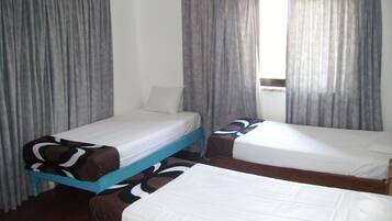 A room with two single beds, a window with curtains, and a wooden floor.