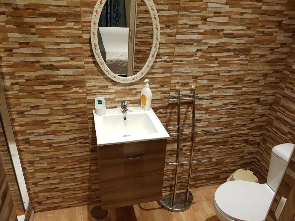 Une salle de bain avec un mur décoré d’un motif imitant la pierre, un lavabo blanc avec un miroir et des toilettes.